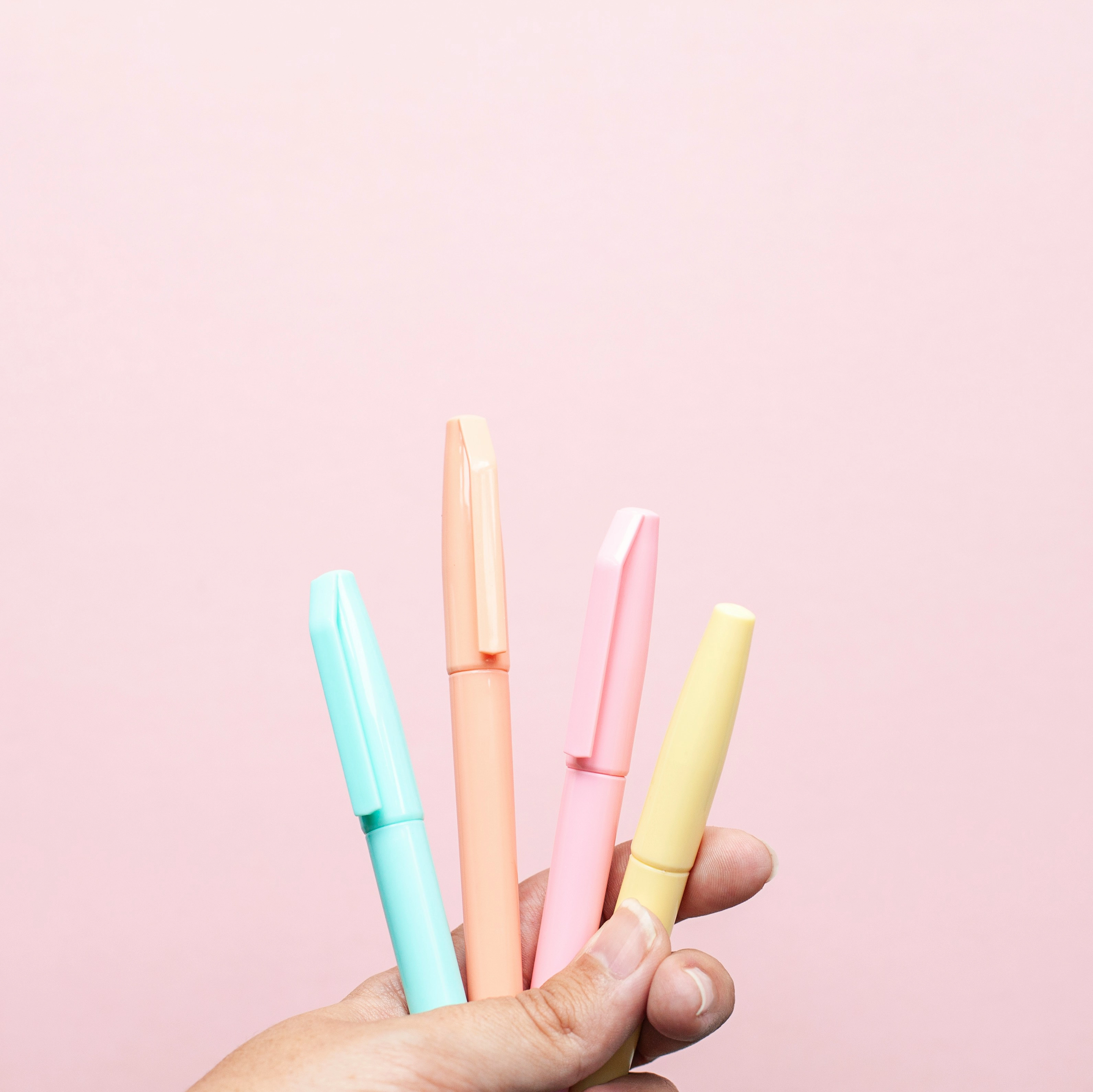 Pastel highlighters held against a pink background